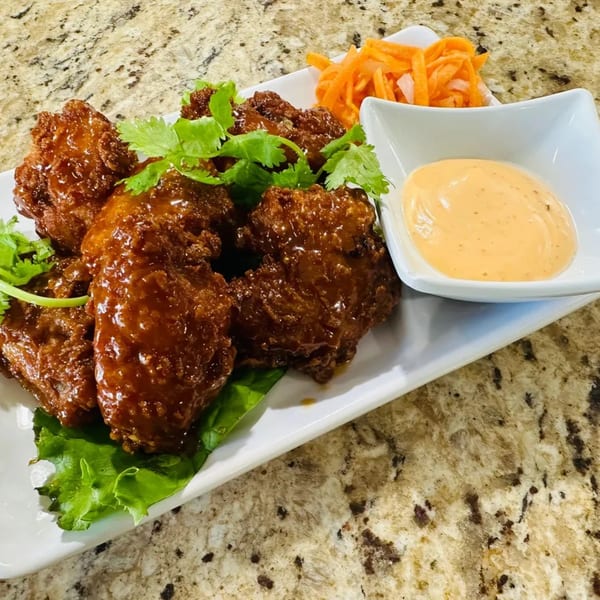 Crispy Vietnamese chicken wings with cilantro, pickled carrots, and a creamy orange dipping sauce.