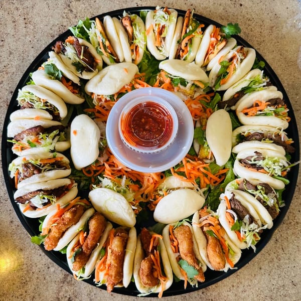 A large platter of assorted Vietnamese bao buns with various fillings and a central dipping sauce.