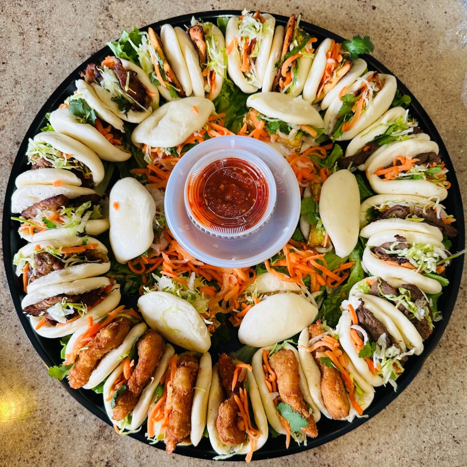A large platter of assorted Vietnamese bao buns with various fillings and a central dipping sauce.