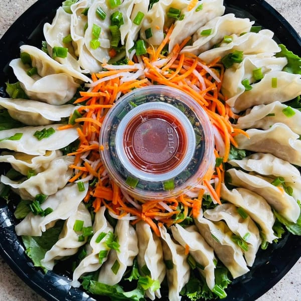A platter of vPho's Vietnamese dumplings, garnished with green onions, shredded carrots, and a dipping sauce.