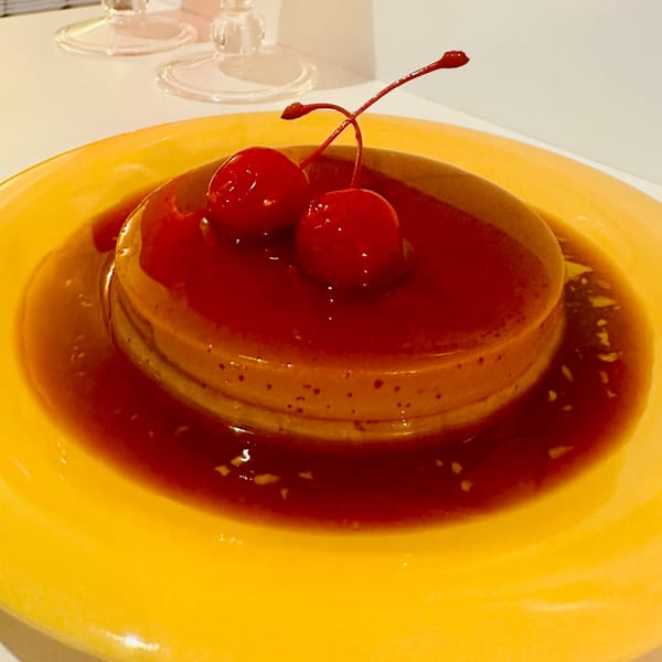 Vietnamese flan dessert with caramel sauce and two bright red cherries on a yellow plate.