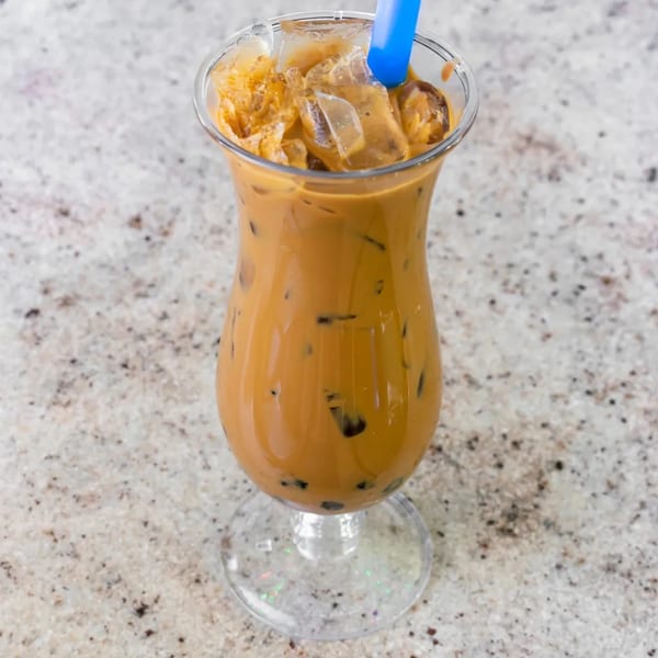 Iced Vietnamese coffee with a blue straw in a tall glass on a speckled countertop.