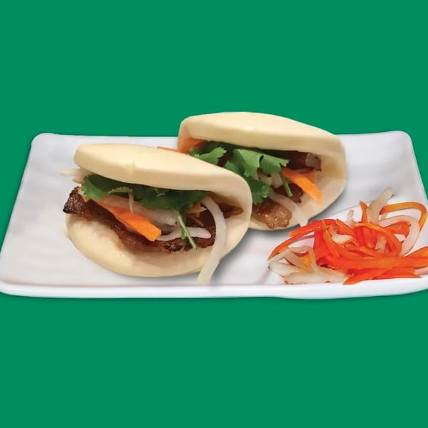 Two Vietnamese bao buns with meat, cilantro, and pickled vegetables on a white plate.