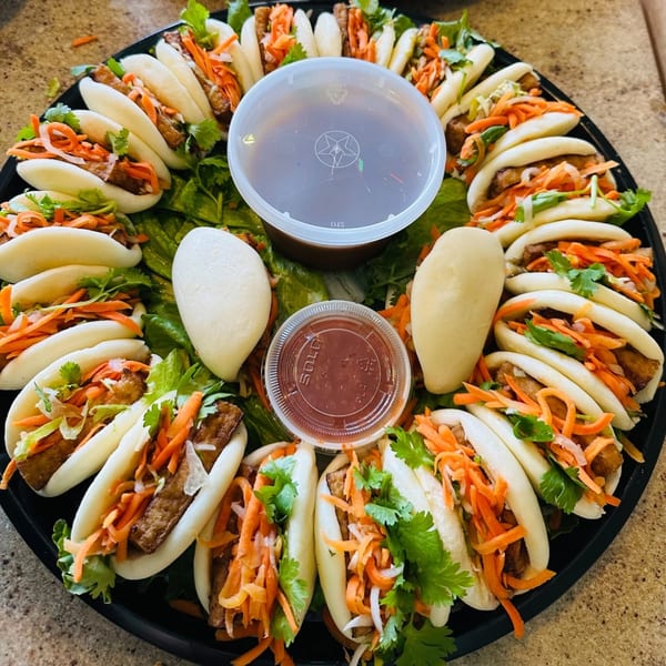 A platter of vPho's Vietnamese bao buns with tofu, carrots, and cilantro, with dipping sauces.