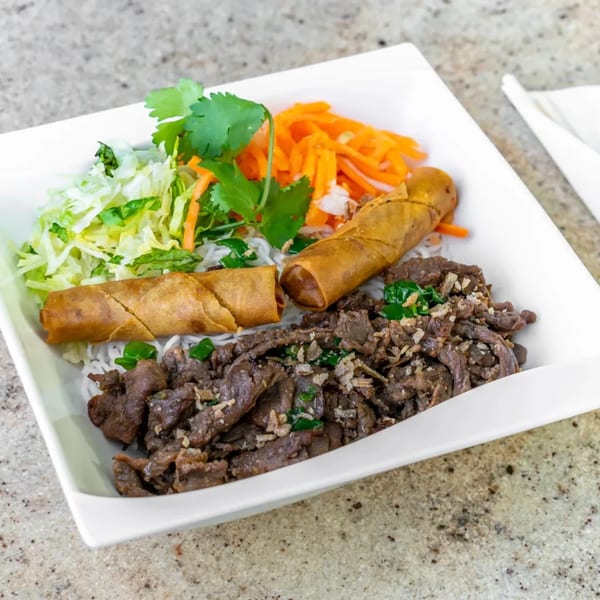 Vietnamese vermicelli bowl with grilled beef, crispy spring rolls, shredded lettuce, and carrots.